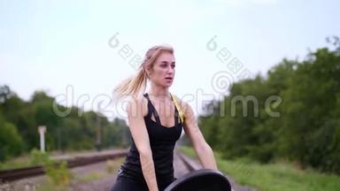 美丽的运动年轻的金发女人，穿着黑色的紧身裤，用一个沉重的盘子做运动，在上面。